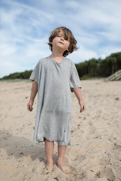 Boy on beach wearing adults t.shirt.