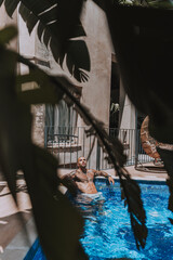 Naklejka na ściany i meble Chico joven musculado y tatuado posando sin camiseta en piscina de estilo boho en un hotel un dia soleado de verano