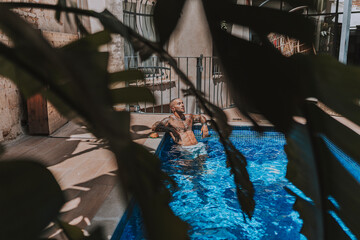 Chico joven musculado y tatuado posando  sin camiseta en piscina de estilo  boho en un hotel un dia soleado de verano