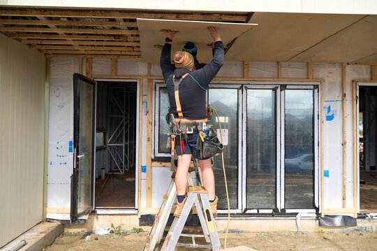 Workers at house build placing cladding 