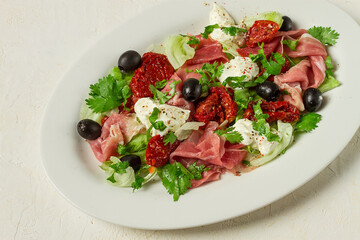 salad with dried tomatoes, prosciutto, soft cheese, olives, homemade, top view,