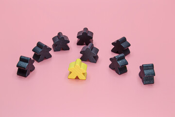 Conceptual image of wooden black toy figures and yellow on a pink background.
