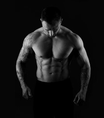 Fototapeta na wymiar Strong man with bare muscular torso, studio black and white photo on black background. Bodybuilder strains body muscles.