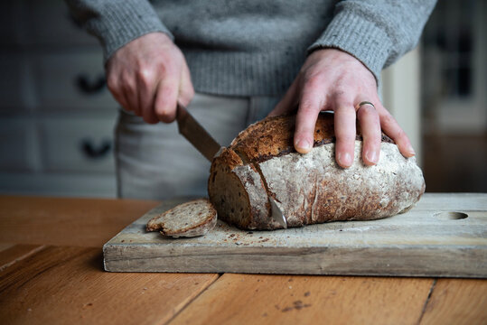 Man in sweater cutting sourdough bread at kitchen table