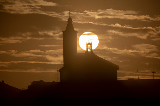 Sun aligned with the silhouette of the church of Luarca, Asturias, Spain