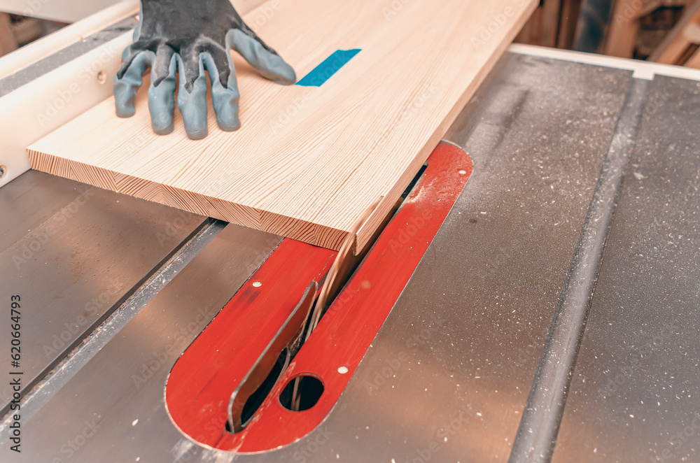 Wall mural the process of cutting a wooden board with a circular saw. a carpenter's hand in a glove.