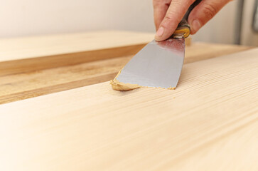 Covering knots on a wooden board with putty. Spatula, putty, wooden board. Carpenter's hands.