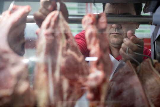 Anonymous butcher hanging fresh meat: view through the glass