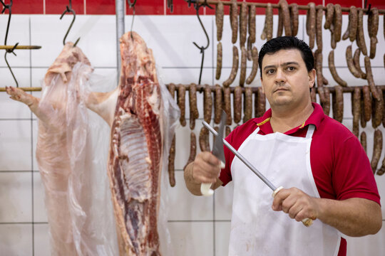 Butcher sharpening blade of knife in front of hanging fresh meat