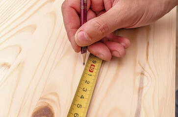 Carpenter's hand writes a marking with a pencil on a wooden board. Centimeter tape.