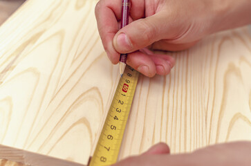 Carpenter's hand writes a marking with a pencil on a wooden board. Centimeter tape.
