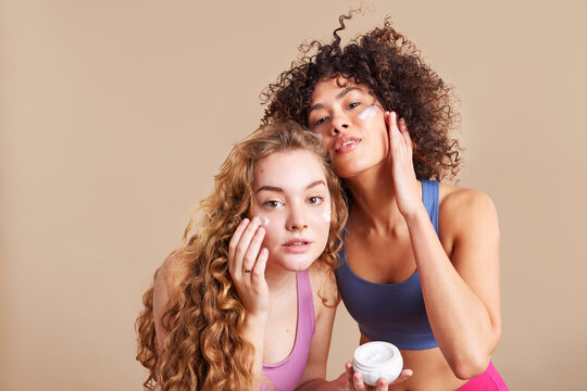 Delighted diverse female models applying cream on faces