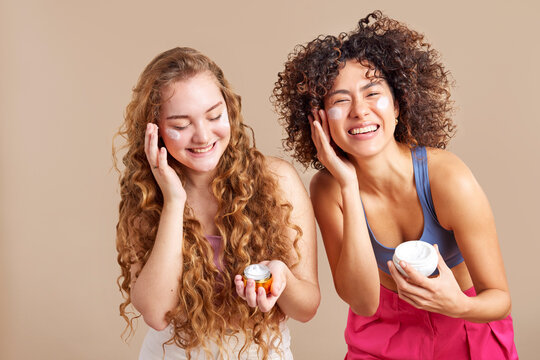 Joyful diverse millennials applying creams on faces