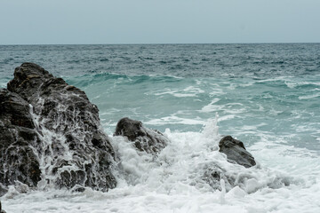 Sea ​​waves crash against a black rock on a cloudy day on the Mediterranean coast in Spain.