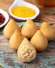 Typical brazilian snack coxinha on a plate with soda glass, ketchup and mustard
