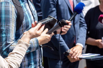 News conference, journalists with microphones and digital voice recorder interviewing politician or...