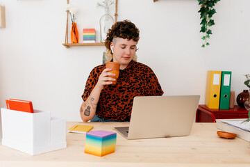 Calm non binary person working on laptop with coffee