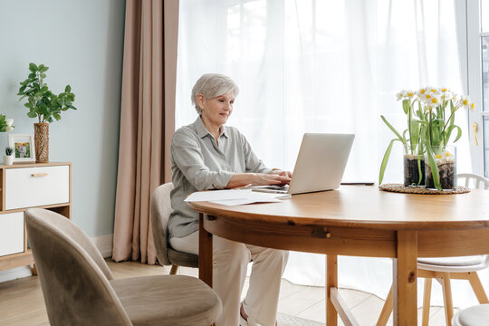 Serious mature woman working on laptop at table