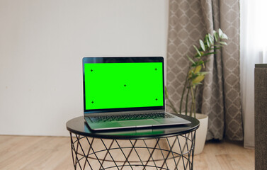 Laptop with green screen on gray coffee table at home