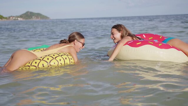 Two women in swimming suits lying on colorful inflatable circles on the water and speaking with ich other. The concept of a summer vacation, trip to the sea, and friendship.