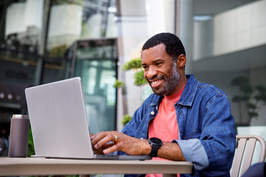 Happy man in denim jacket working in front of laptop