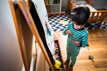 Boy paints at easel in bedroom