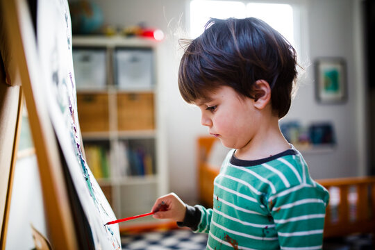 Boy paints at easel in bedroom