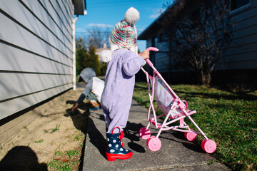 Toddler walks down sidewalk pushing doll stroller