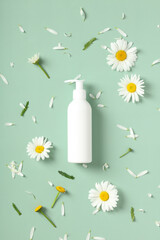 Empty white cosmetic bottle with pump and daisy flowers on green background. SPA beauty product...
