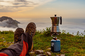 first person view of the legs of a mountain hiker preparing a coffee in an Italian coffee maker with a camping stove at sunrise. sport and adventure. backpacker.