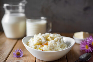 Delicious breakfast: rice porridge with butter and milk in a white plate on a wooden background. Close-up