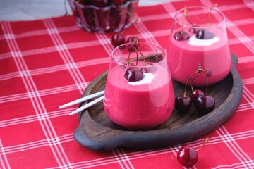 Cold cherry summer soup Meggyleves with cream and whole cherries in glass goblets on a table with a red tablecloth. 