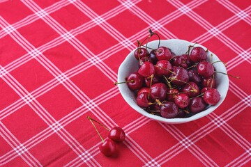 Ripe juicy cherries with water drops in a ceramic bowl on a table with a red tablecloth. Summer berries.