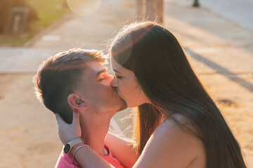 joven pareja dándose un precioso beso durante el atardecer en el parque bañada por los...