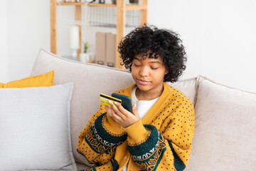 African american woman shopping online holding smartphone paying with gold credit card. Girl sitting at home buying on Internet enter credit card details. Online shopping ecommerce delivery service