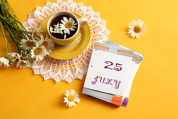 Calendar for July 25: the name of the month July in English, the numbers 25, a cup of tea on an openwork napkin with chamomile, next to a bouquet of daisies, yellow background