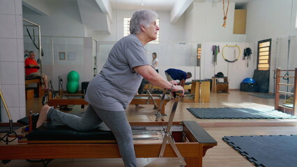 Older woman using Pilates Machine to stretch body. Elderly person workout routine