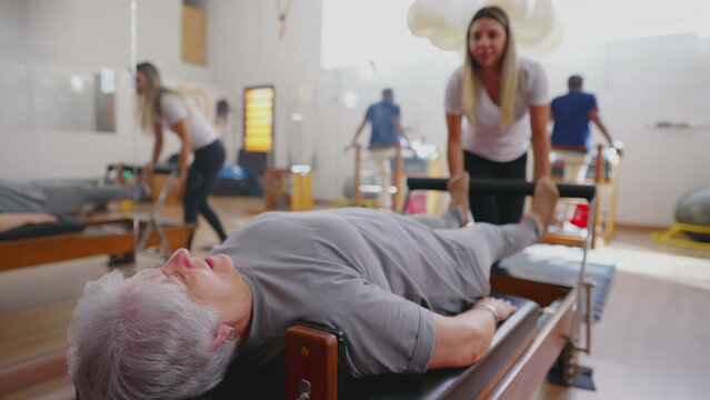 Older woman exercising in Pilates Studio Session. An elderly caucasian person laid on Machine stretching body with the guidance of Coach instructing exercise