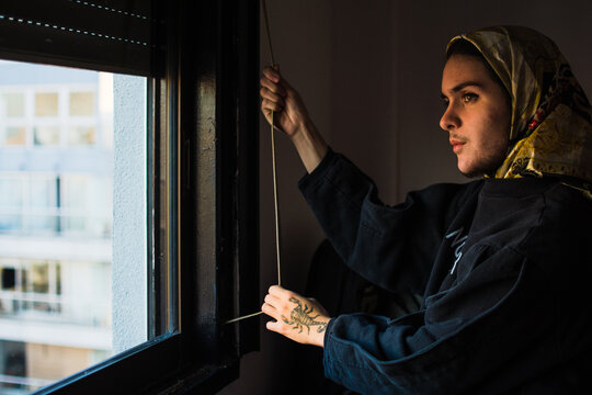 Trans muslim person opening blinds at sunrise