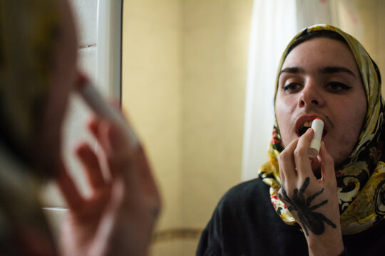 Queer person looking in the mirror applying lipgloss