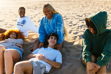 Happy diverse friends sitting on sandy beach