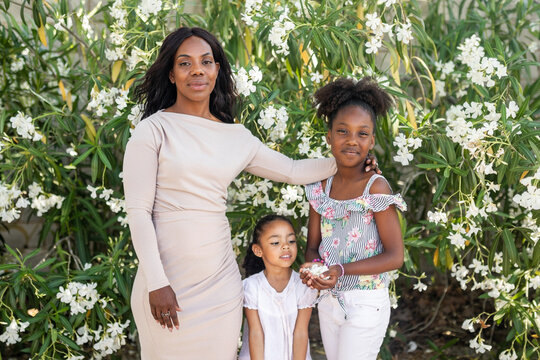 Black Mother With Daughters Outdoors On A Background Of White Flowers