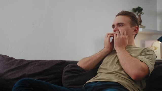 The guy gloomily watches TV, engaging in passive entertainment by consuming content.