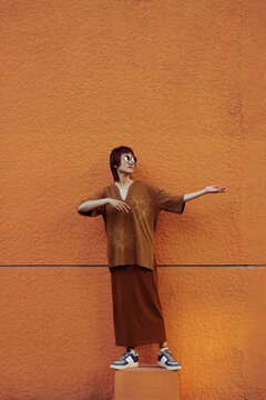 Woman Envisions Violin in playful pose by Orange Wall