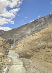Beautiful view of a wooden suspension bridge over river in between dry mountains in Ladakh, INDIA.