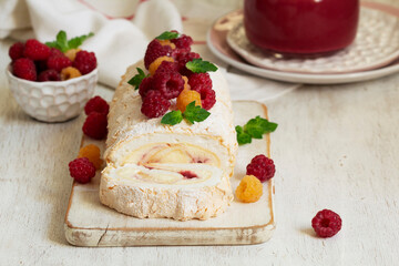 Meringue roll with butter cream and raspberry curd, decorated with berries on a light background.