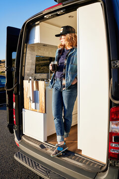 Portrait of woman camping in camper van in nature drinking coffee