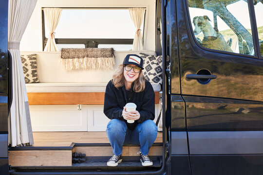Portrait of woman smiling with coffee and dog in camper van traveling