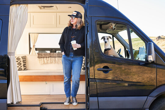 Portrait of woman with coffee and dog on road trip luxury camper van
