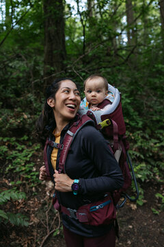 Smiling woman and baby in carrier outside in forest.